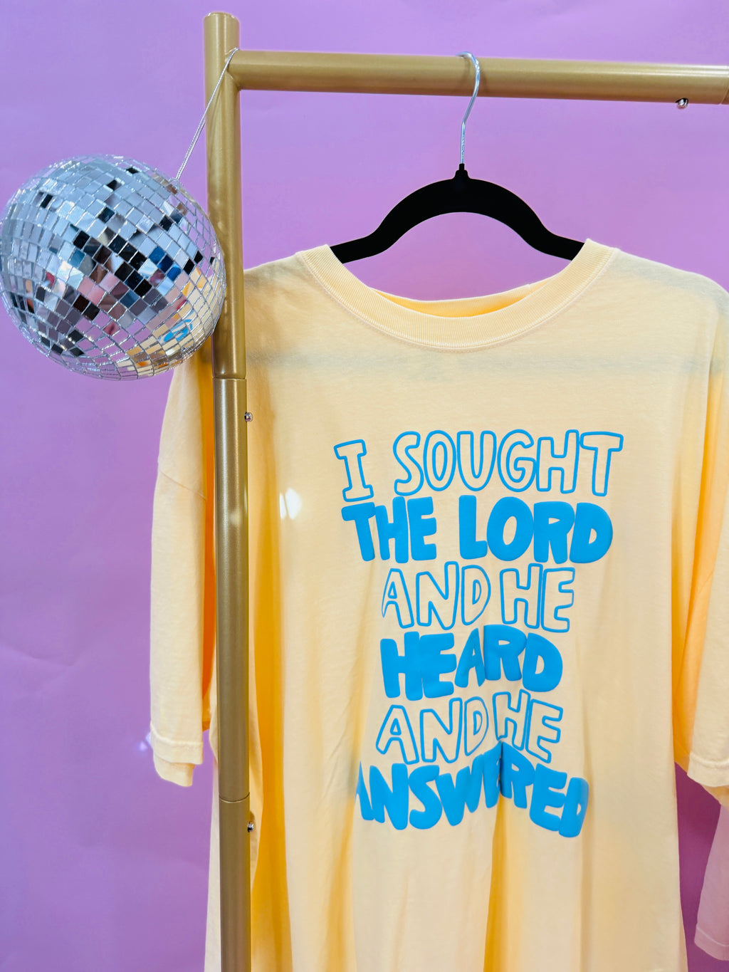 Buttery yellow shirt with blue puff lettering that says “I sought the Lord, He heard, and He answered” Christian graphic tee