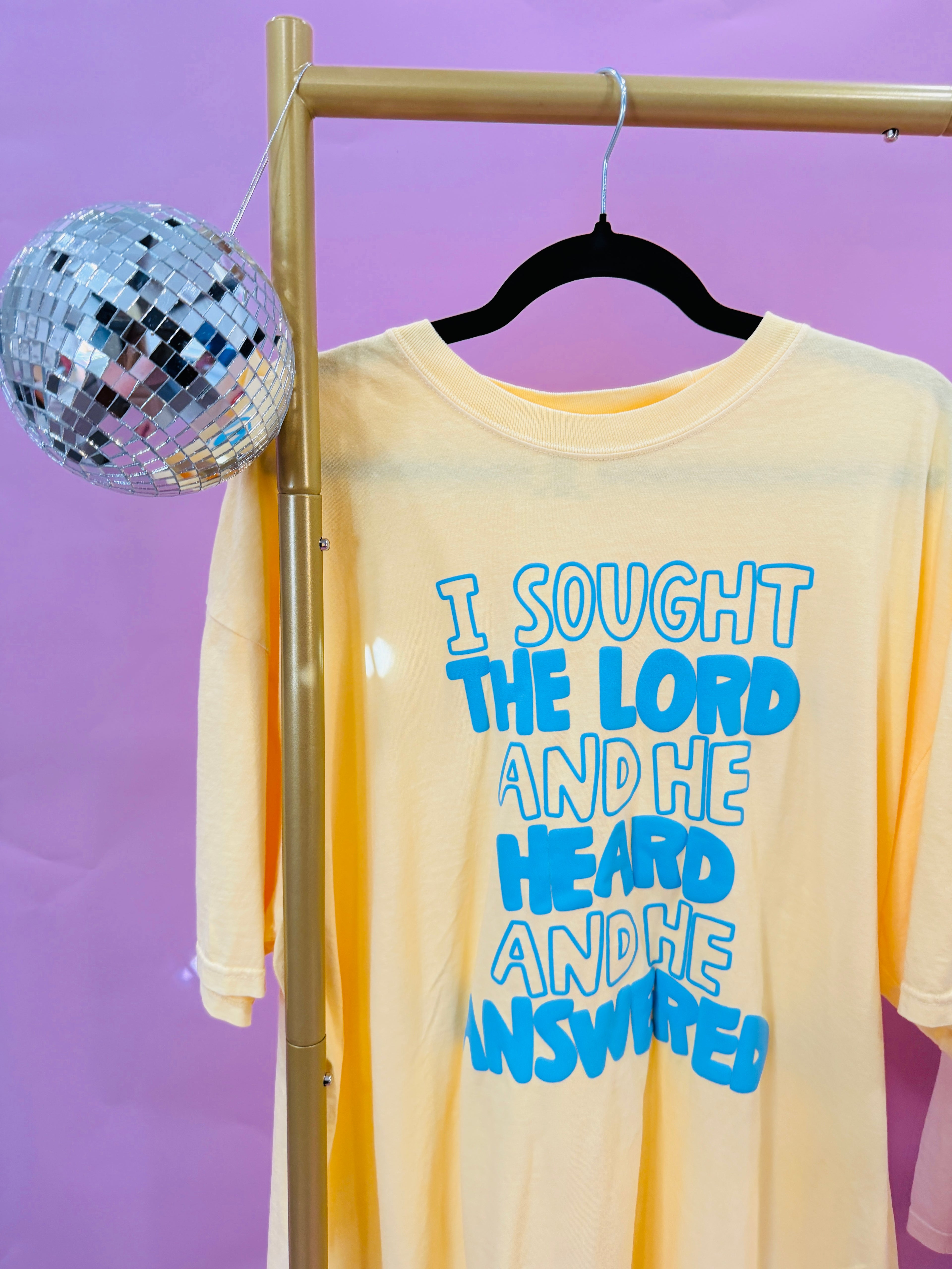 Buttery yellow shirt with blue puff lettering that says “I sought the Lord, He heard, and He answered” Christian graphic tee